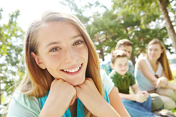 Image showing Feeling secure in her familys love. A pretty young girl sitting outdoors in the park with her family in the background.