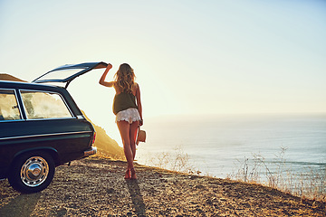 Image showing On the hunt for wild open spaces. Rearview shot of a young woman standing next to her car during a roadtrip.