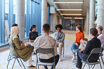 Image showing A diverse group of young business entrepreneurs gathered in a circle for a meeting, discussing corporate challenges and innovative solutions within the modern confines of a large corporation