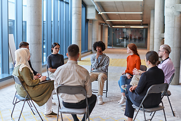 Image showing A diverse group of young business entrepreneurs gathered in a circle for a meeting, discussing corporate challenges and innovative solutions within the modern confines of a large corporation