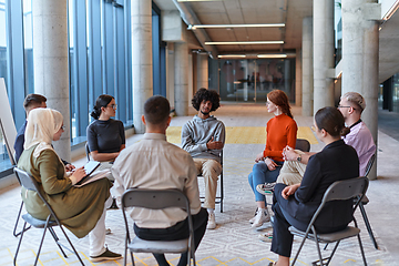 Image showing A diverse group of young business entrepreneurs gathered in a circle for a meeting, discussing corporate challenges and innovative solutions within the modern confines of a large corporation