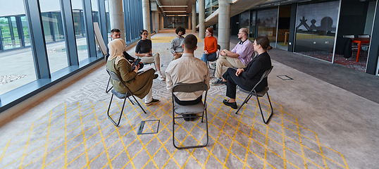 Image showing A diverse group of young business entrepreneurs gathered in a circle for a meeting, discussing corporate challenges and innovative solutions within the modern confines of a large corporation