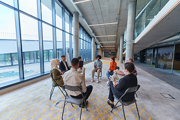 Image showing A diverse group of young business entrepreneurs gathered in a circle for a meeting, discussing corporate challenges and innovative solutions within the modern confines of a large corporation