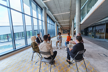 Image showing A diverse group of young business entrepreneurs gathered in a circle for a meeting, discussing corporate challenges and innovative solutions within the modern confines of a large corporation