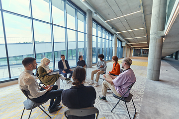 Image showing A diverse group of young business entrepreneurs gathered in a circle for a meeting, discussing corporate challenges and innovative solutions within the modern confines of a large corporation