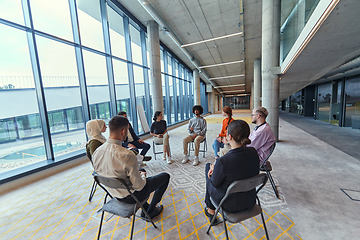 Image showing A diverse group of young business entrepreneurs gathered in a circle for a meeting, discussing corporate challenges and innovative solutions within the modern confines of a large corporation