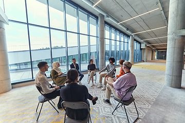 Image showing A diverse group of young business entrepreneurs gathered in a circle for a meeting, discussing corporate challenges and innovative solutions within the modern confines of a large corporation