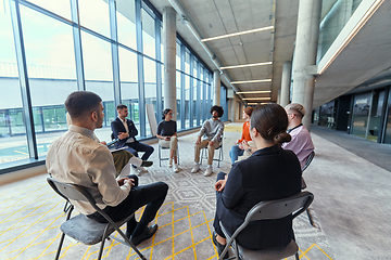 Image showing A diverse group of young business entrepreneurs gathered in a circle for a meeting, discussing corporate challenges and innovative solutions within the modern confines of a large corporation