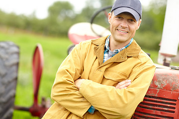 Image showing Another good days work. Portrait of a smiling farmer with his arms crossed standing infront of his tractor.