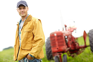 Image showing Im at my happiest while doing what I love. Portrait of a farmer standing in a field with a tractor behind him.