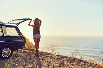 Image showing This is where she comes to unwind. Rearview shot of a young woman standing next to her car during a roadtrip.