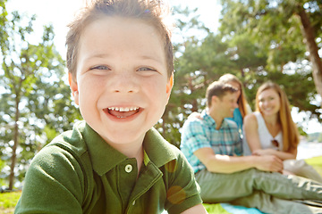 Image showing Enjoying family time in the park. A happy little boy sitting outdoors with his family on a sunny day.