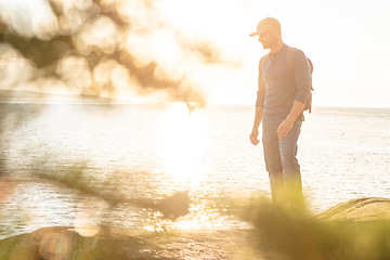 Image showing Every new trail is a new adventure. a man wearing his backpack while out for a hike on a coastal trail.