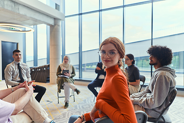 Image showing A diverse group of young business entrepreneurs gathered in a circle for a meeting, discussing corporate challenges and innovative solutions within the modern confines of a large corporation