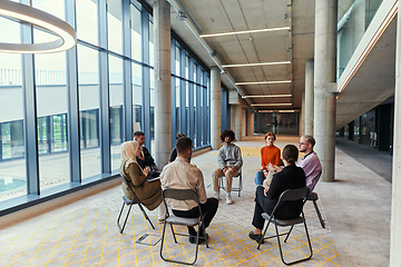 Image showing A diverse group of young business entrepreneurs gathered in a circle for a meeting, discussing corporate challenges and innovative solutions within the modern confines of a large corporation