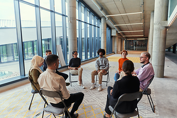 Image showing A diverse group of young business entrepreneurs gathered in a circle for a meeting, discussing corporate challenges and innovative solutions within the modern confines of a large corporation