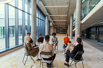 Image showing A diverse group of young business entrepreneurs gathered in a circle for a meeting, discussing corporate challenges and innovative solutions within the modern confines of a large corporation