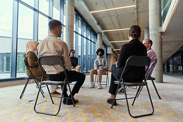 Image showing A diverse group of young business entrepreneurs gathered in a circle for a meeting, discussing corporate challenges and innovative solutions within the modern confines of a large corporation