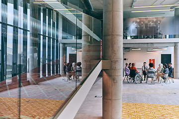 Image showing A diverse group of young business entrepreneurs gathered in a circle for a meeting, discussing corporate challenges and innovative solutions within the modern confines of a large corporation