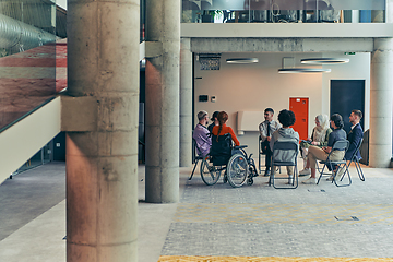 Image showing A diverse group of young business entrepreneurs gathered in a circle for a meeting, discussing corporate challenges and innovative solutions within the modern confines of a large corporation