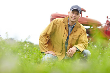 Image showing Being a farmer is part of who I am. Portrait of a farmer kneeling in a field with his tractor parked behind him.