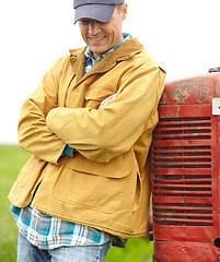 Image showing Living a good and simple life. a smiling farmer standing next to his tractor with his arms crossed and looking down.