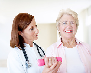 Image showing Buoyed by her progress. Determined elderly female is assisted by her nurse as she lifts a dumbbell.