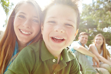 Image showing Shes a caring big sister. A happy little boy sitting outdoors with his family on a sunny day.