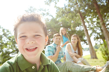 Image showing He loves spending time with his family. A happy little boy sitting outdoors with his family on a sunny day.