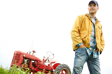 Image showing Taking in the beauty of my farm. a farmer standing in a field with a tractor parked behind him.