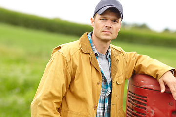 Image showing Serious about farming. Portrait of a serious farmer with his arm resting on the hood of his tractor while he stands in an open field.