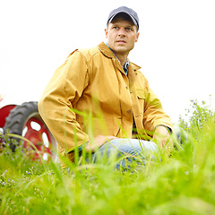 Image showing Lost in thought. A farmer kneeling in a field with his tractor parked behind him.