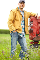 Image showing Taking a moment to relax. Portrait of a man standing in a field with his arm resting on the hood of a tractor.