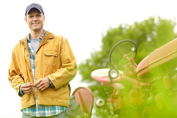 Image showing Hes happiest on the farm. Portrait of a smiling farmer standing next to his tractor in a field.