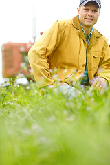 Image showing My passion lies in farming. Portrait of a farmer kneeling in a field with his tractor parked behind him.