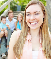 Image showing One happy mother and wife. Smiling attractive mother with family sitting behind her while outdoors.