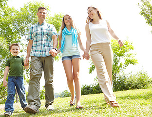 Image showing Family time spent outdoors. A happy young family walking through the park together on a summers day.