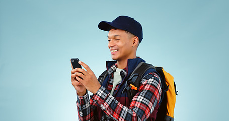 Image showing Hiking, smile and typing with man, cellphone and adventure with social media on blue studio background. Person, hiker and model with a smartphone, mobile user and contact with journey or mockup space