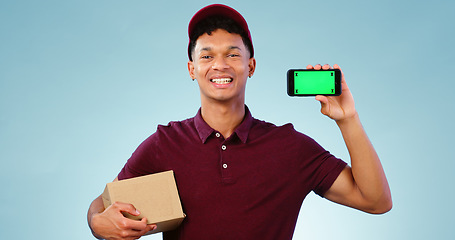 Image showing Courier man, phone and green screen in studio for smile, mockup space or box by blue background. Supply chain expert, cardboard package and smartphone for app promotion, chromakey or tracking markers