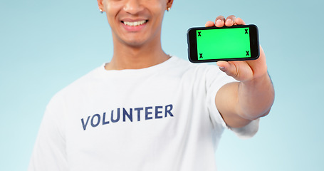Image showing Hand, phone and green screen with a volunteer man in studio on blue background for marketing or charity. Smile, space or advertising and a person showing chromakey on a display with tracking markers