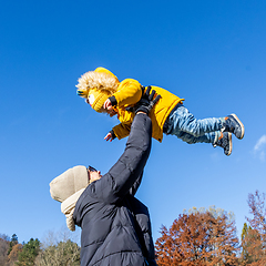 Image showing More, more,...mum, that's fun. Happy young mother throws her cute little baby boy up in the air. Mother's Day, Mather and her son baby boy playing and hugging outdoors in nature in fall.