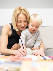 Image showing Caring young Caucasian mother and small son drawing painting in notebook at home together. Loving mom or nanny having fun learning and playing with her little 1,5 year old infant baby boy child.
