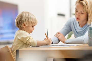 Image showing Caring young Caucasian mother and small son drawing painting in notebook at home together. Loving mom or nanny having fun learning and playing with her little 1,5 year old infant baby boy child.