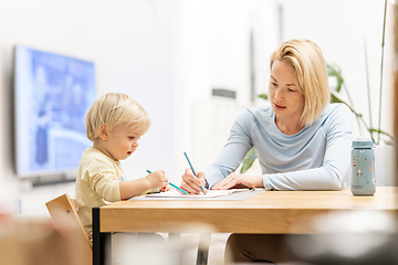 Image showing Caring young Caucasian mother and small son drawing painting in notebook at home together. Loving mom or nanny having fun learning and playing with her little 1,5 year old infant baby boy child.