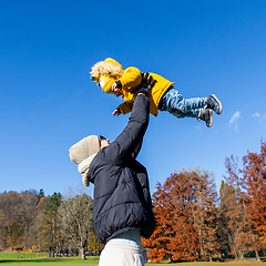 Image showing More, more,...mum, that's fun. Happy young mother throws her cute little baby boy up in the air. Mother's Day, Mather and her son baby boy playing and hugging outdoors in nature in fall.