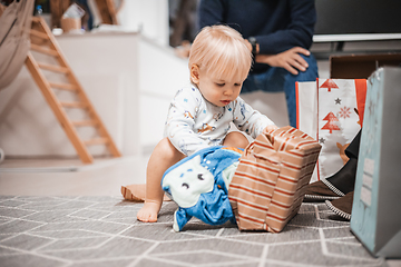 Image showing Cute little blond Caucasian toddler unpacking Christmas or Birthday present. Adorable small infant baby boy opening gift