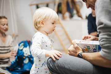 Image showing Cute little blond Caucasian toddler unpacking Christmas or Birthday present. Adorable small infant baby boy opening gift