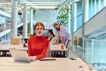 Image showing In a modern startup office, a professional businesswoman with orange hair sitting at her laptop, epitomizing innovation and productivity in her contemporary workspace.