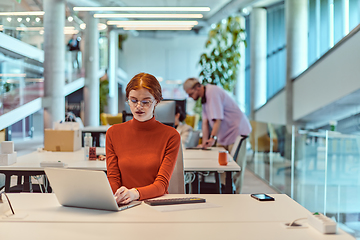 Image showing In a modern startup office, a professional businesswoman with orange hair sitting at her laptop, epitomizing innovation and productivity in her contemporary workspace.