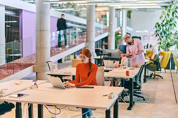 Image showing In a modern startup office, a professional businesswoman with orange hair sitting at her laptop, epitomizing innovation and productivity in her contemporary workspace.